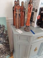 Four wooden figures from Southern Living collection displayed on a light gray cabinet, including three men in robes and one angel figure, with visible wear and packing material suggested.