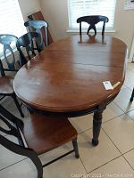 Full view of wooden kitchen table with leaf attached and surrounding chairs under natural light.