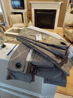 Folded gray drapery panels stacked, showing metal grommets and fabric texture.