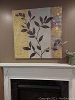 Frontal photo of the 39x39 canvas artwork showing leaf and floral patterns in earthy and gold tones above a white mantelpiece.
