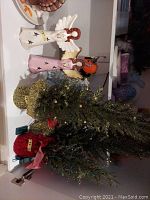 Three battery-powered artificial trees with gold decorative fabric bases along with two ceramic angel figurines on a white shelf.