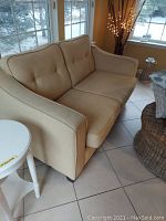 Beige fabric loveseat positioned near windows with visible slight stains and scuffs.