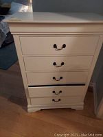 Front view of white dresser showing five drawers with metal handles; one drawer partially open.