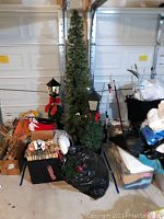 Photo showing the 6.5 ft tall narrow artificial Christmas tree, two black lamp post lantern light decorations with red bows, and assorted Christmas decor in boxes.
