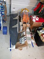 Photo of shelf, ironing board, Sea Sand Surf sign, woven scarecrow and other wooden items laid on a floor