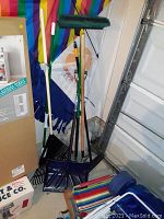 Group of yard tools including rake, shovels, and brooms in corner of garage.