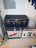 Front view of a navy blue foot locker trunk with brass hardware sitting on boxes, showing latch closures and handle.