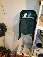 Stack of four dark green metal folding chairs with padded, dark fabric seats and backs, showing dotted upholstery pattern.