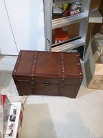 Closed rectangular trunk with leather top and front, with metal rivets and a metal clasp lock on front.