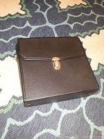 Closed black carrying case with snap clasp for the binoculars, shown on blue and beige carpet.