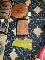 Photo showing both the round wine barrel top cheeseboard and the rectangular cork tray filled with corks on a patterned floor.
