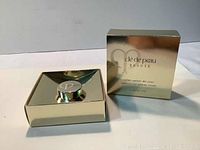 Photo showing the product box and jar with reflective gold surfaces and Clé de Peau Beauté branding.