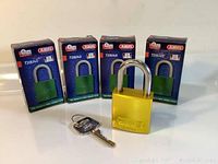 Four new ABUS padlocks with gold-colored solid aluminum bodies in original blue boxes. One padlock and one key shown outside their boxes.