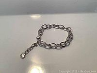 Silver rhodium plated oval link charm bracelet shown on reflective surface highlighting chain and crystal charm details.