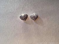 Front view of the pair of heart-shaped earrings with clear crystals in pave setting on rhodium plated base.