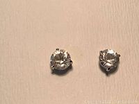 Pair of Swarovski solitaire stud earrings with clear round crystals set in white rhodium plated prong settings shown on textured beige background.