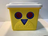 Yellow square plastic bucket with an owl face design featuring red eyes and blue beak, shown alone.
