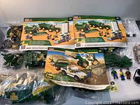 Photo shows two instruction manuals for John Deere Mega Bloks sets and unopened bags of plastic pieces, figures, and small parts laid out on a flat surface.