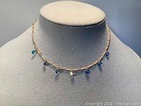 Golden chain choker necklace with small iridescent beads on a display bust, showing design and bead spacing.