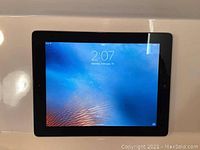 Front view of Apple iPad 2 with screen on showing lock screen time and wallpaper.