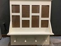 Full front view showing the photo frame board with all eight openings, the shelf immediately below, and the four white hanging hooks at the bottom.