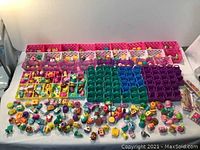 Overview of the entire lot showing multiple rows of pink, white, purple and translucent storage baskets with numerous colorful Shopkins figures placed on and around them, along with green and purple display racks.