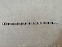 Overall view of the full length silver-toned bracelet with alternating clear rhinestone clusters and dark blue rectangular gemstones on a neutral background.