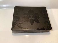 Stack of 8 black square leather coasters showing embossed floral pattern in foil
