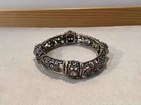 Side angle of vintage elastic bracelet showing ornate silvery metal patterns and rhinestone clusters embedded in round sections.