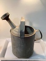 Side view of galvanized watering can showing handle, spout, and body surface.