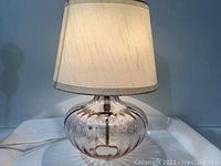 Front view of the lamp showing the rounded transparent glass base and beige fabric lamp shade.