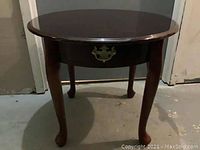 Front view of round end table showing Queen Anne legs and small single drawer with decorative metal pull