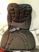 Full view of the black padded heat and massage seat cushion showing the backrest and seat sections with the controller and power adapter placed on the seat portion.