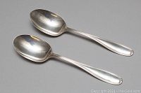 Two sterling silver serving spoons displayed top side up, showing polished bowls and handles