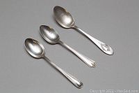 Three sterling silver spoons arranged side by side, showing varied handle designs and overall condition.