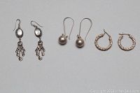 A photo showing all three pairs of silver earrings laid side by side: dangle mother of pearl earrings, silver ball drop earrings, and small textured silver hoops.