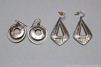 Two pairs of earrings displayed side by side, the round hoop pair on the left and the triangular etched pair on the right.