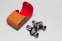 TASCON opera glass style binoculars shown outside and inside the brown leather case with red interior.