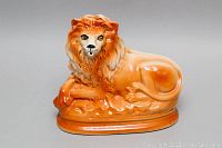 Front angled view of orange glazed Staffordshire lion sculpture showing facial details and mane.