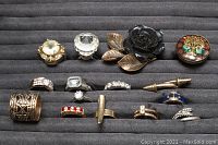 Top-down view of 15 assorted costume rings in rows on grey jewelry display pad. Shows variety in styles, colors, and sizes.