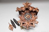 Front view of cuckoo clock case with carved leaf motif and dial, weights and pendulum laid next to it
