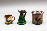 Three Royal Torquay pottery pieces displayed front-facing showing rooster motifs and inscriptions.