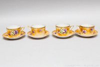 Four hand painted Nippon teacups and saucers displayed in a row, each with yellow-orange background and purple and white floral decoration.