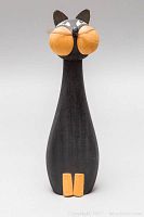 Front angle of wooden cat sculpture showing black body, orange cheeks and paws, with painted eyes and nose detail.