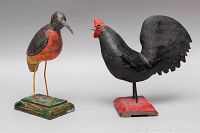 Two wooden bird folk art sculptures displayed side by side on a grey surface, one rooster and one smaller bird.