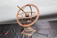 Full view of the rusty cast metal armillary sundial on a black background showing its concentric rings and base.
