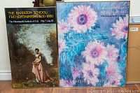Photo showing both framed posters side by side on the floor against a wall, displaying art from Barbizon School and Impressionist-themed floral art