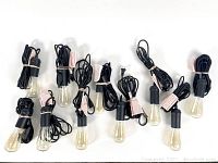 10 Edison bulbs with attached black pendant cords coiled and secured with tags, laid out on flat surface.