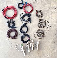 Shows 12 extension cords neatly coiled, three are brown 12ft with 2-prong plugs, six are black 15ft with 3-prong plugs, two are red 25ft with 3-prong plugs, plus 4 white power strips each with 3 outlets.