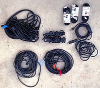 All items laid out on concrete surface showing two power strips and eight extension cords of various lengths, all black with 3-prong plugs.